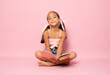 © Danko - Portrait of a smiling little girl sitting with legs crossed, studying isolated over pink background