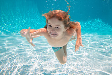 Wall Mural - Kid boy swimming underwater. Kid in the water swimming under water and smiling. Child swim underwater in pool. Funny happy kids face.