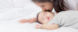 © NT_studio - Young asian mother kiss cheek of little baby girl with tender on bed in the bedroom, mom love newborn and care, mother with expression with child together, parent and daughter, family concept.