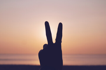 Wall Mural - Peace out or fighting metaphor two fingers hand sign in front of a sunset.