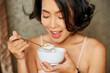 © DragonImages - Happy young woman enjoying delicious granola with greek yogurt for breakfast