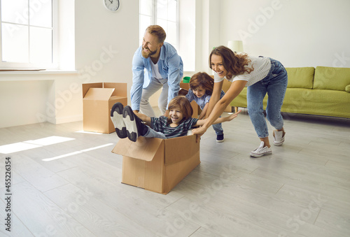 Happy family having fun in new home. Joyful excited first-time buyers with children playing with cardboard boxes in living room interior. Real estate, residential mortgage, buying dream house concept