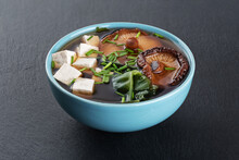 Miso Soup With Shiitake Mushrooms, Tofu Cheese, Fresh Onions And Wakame Seaweed On A Slate Board Background.