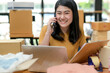 © sarawutnirothon - A woman selling an online product talks on the phone for information and holds a customer file.