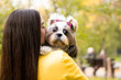 A brunette woman holds in her arms hugs and kisses a funny surprised shih tzu dog in  autumn park. copy space background. The concept of love and care for animal