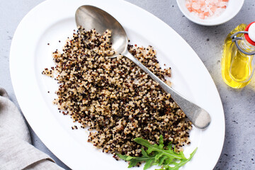 Cooked white, red and black quinoa in white plate on grey rustic background, top view, place for text recipes or menu. Vegan Superfood, healthy eating and nutrition or diet concept.