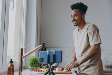 Canvas Print - Young minded happy african american man in casual clothes prepare sweet breakfast cut fruit do selfie shot mobile cell phone cook food in indoor kitchen at home alone Healthy diet lifestyle concept