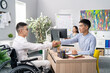 © ABCreative - Two men meet in company office morning for interview disabled boy arrives in wheelchair wearing white shirt boss sitting across from him shakes hands to greet him goodbye congratulate on getting job