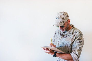 Wall Mural - Caucasian man in camouflaged military uniform writing in notebook.