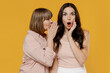 Two young confused daughter mother together couple women wearing casual beige clothes whisper gossip and tell secret behind her hand sharing news isolated on plain yellow background studio portrait