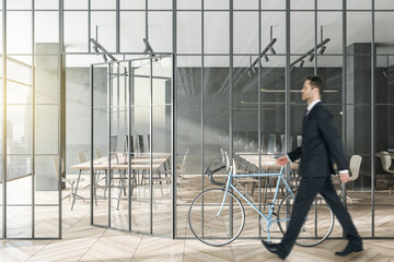 Aufkleber - Businessman walking in modern glass partition and bike in stylish coworking office interior with city view and daylight.