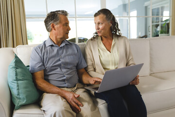 Wall Mural - Happy senior caucasian couple in living room, sitting on sofa, using laptop