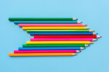 Сolored pencils folded in the shape of an arrow indicating the direction on blue background. Concept of diversity, connection, and movement in one direction.
