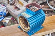Burnt out electric engine with light blue metal case stands on long wooden board on waste products background close view