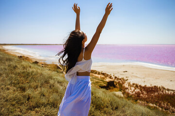 Wall Mural - Beautiful asian women tourist in white long dress walking in water on pink salt Lake. 