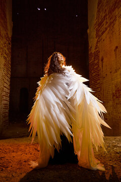 A brunette girl with long hair and white wings in an evening dress in a vintage Gothic castle. Woman who looks like an witch or angel in an abandoned old church. Female Model posing in dark hall