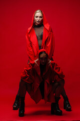 two slender young and attractive girls in red raincoats with a hood on a red background in a photo studio