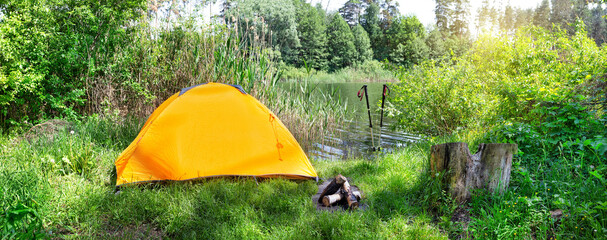 Wall Mural - orange tent on background of river and trekking poles on summer day
