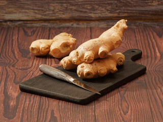 Wall Mural - Ginger root and a knife on a burned wood cutting board over brown wood background