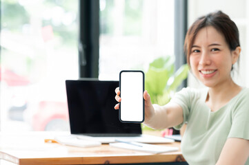 Wall Mural - young asian woman showing blank screen smartphone while sitting at the table in living room.
