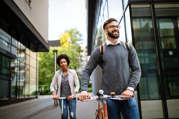 Two smiling business people driving electric scooter, bicycle going to work.