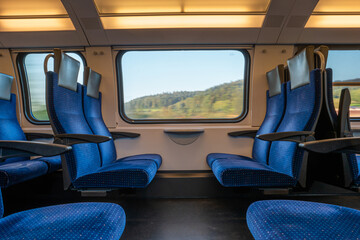 blue empty opposing seats in a moving train. large window with blurred landscape, daytime, summer, n