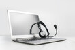 © taniasv - Side view of slim laptop with headphones headset on white desk. Monochrome background. Distant learning. working from home, online courses or support. Audio podcast. Helpdesk or call center banner