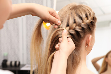 professional stylist braiding client's hair in salon