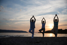 Group Of People Practice Tai Chi Chuan  At Sunset On The Beach.  Chinese Management Skill Qi's Energy.