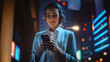 © Gorodenkoff - Beautiful Young Woman Using Smartphone Standing on the Night City Street Full of Neon Light. Portrait of Gorgeous Smiling Female Using Mobile Phone.