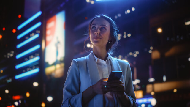 Fototapete - Beautiful Young Woman Using Smartphone Standing on the Night City Street Full of Neon Light. Portrait of Gorgeous Smiling Female Using Mobile Phone.