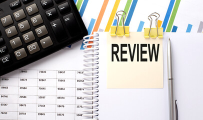 Poster - REVIEW text, written on a sticker with calculator,pen on chart background.