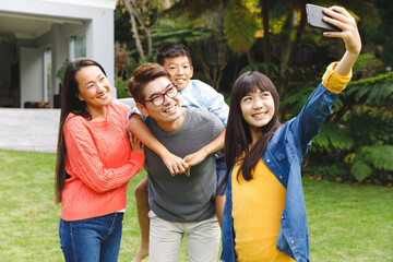 Wall Mural - Happy asian parents, son and daughter smiling outdoors and taking selfie in garden