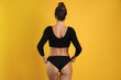 Woman in black sexy panties on yellow background, back view
