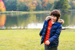 © Anna - Young boy enjoying a walk in the autumn park near beautiful lake with reflections. Child wearing warm jacket smiling and playing outdoors. Golden fall weather.