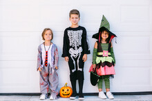 Children In Halloween Costumes Standing Near Wall And Looking At Camera