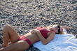 Woman relaxing laying on the pebble beach wearing pink bathing suit