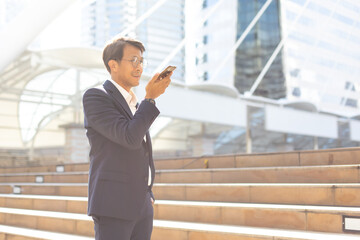 Wall Mural - Asian businessman using mobile phone app texting outside the office building