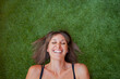 © Sophiaarenasphoto - Mujer sonriendo echada sobre su espalda en el cesped verde. Mujer de pelo marrón y camiseta de tirantes negro. Retrato de chica
