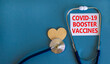 Covid-19 booster shots vaccines symbol. White card with words Covid-19 booster vaccines, beautiful blue background, wooden heart and stethoscope. Covid-19 booster shots vaccines concept.