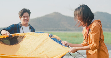 Young asia campers couple setting up the tent camping gear outdoor near seaside. Male and female travel having fun on a summer day at campsite. Outdoor activity, adventure travel, or holiday vacation.