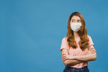 Young Asia girl wearing medical face mask with dressed in casual cloth and looking at blank space isolated on blue background. Self-isolation, social distancing, quarantine for corona virus prevention