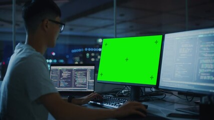 Wall Mural - Night Office: Young Japanese Man in Working on Green Screen Chroma Key Desktop Computer. Team of Programmers Typing Code, Creating Modern Software, e-Commerce App Design, e-Business Programming
