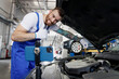 Young troubleshooter technician car mechanic man in blue overalls white t-shirt talk mobile cell on phone stand show thumb up fix problem with raised hood work in vehicle repair shop workshop indoors