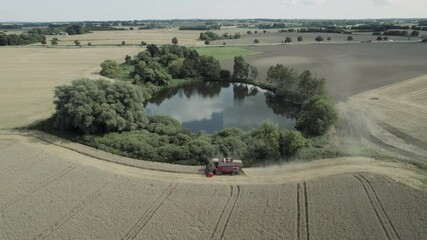 Wall Mural - aerial tracking shot of harvester harvests in the field close to a lake agriculture road with cars i