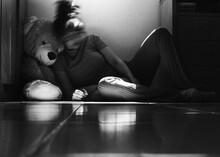 Grayscale Photo Of A Woman Sitting Between A Wooden Cabinet And A Teddy Bear