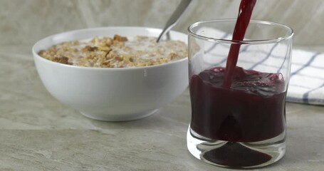 Sticker - Pouring cranberry juice in a glass next to a bowl of almond granola slow motion