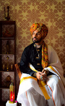 Man Wearing Traditional Dress Sitting On Chair Beside Display Cabinet