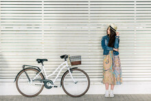 Woman In Floral Dress Leaning On Light Wall Beside Light Bicycle