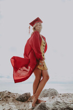 Woman In Red Graduation Gown Standing On Seashore During Daytime